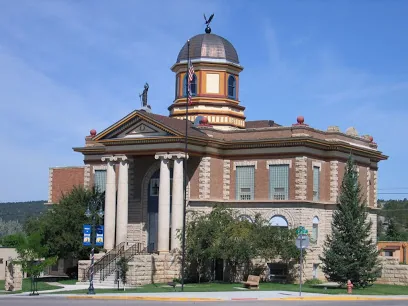 Red brick courthouse with white columns, dome, and cupola under blue sky with trees and landscaping in foreground