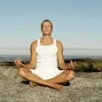 Person sitting in lotus position on sandy ground with clear sky and landscape in background